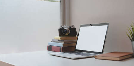 Open blank screen laptop computer with coffee cup and office supplies in comfortable workplace near the windowsの写真素材