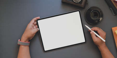 Overhead shot of young man working on blank screen tablet in dark trendy workspace and coffee cupの写真素材