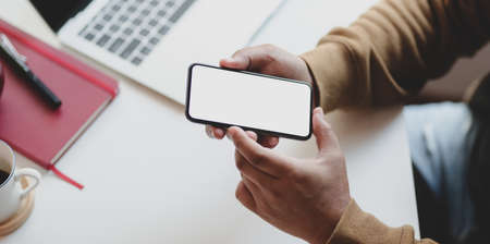 Close-up view of young man working on his project while looking for new information on blank screen smartphoneの写真素材