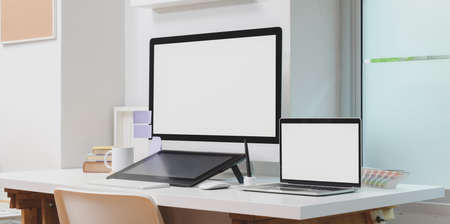 Blank screen desktop computer and laptop computer with office supplies in modern workspaceの写真素材