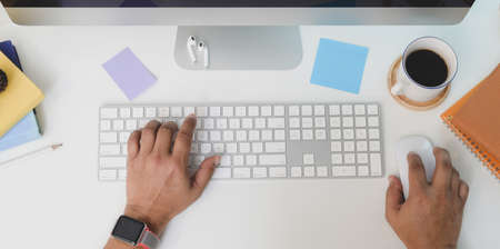 Top view of young man typing on keyboard computer while working on his project with coffee cupの写真素材