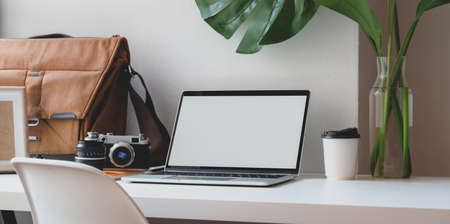 Comfortable workspace with blank screen laptop computer with mailbag and office supplies next to the windowsの写真素材