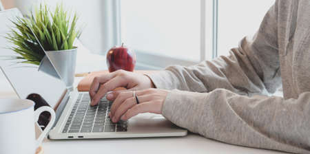 Close-up view of young female typing on laptop computer in comfortable workspace near the windowsの写真素材