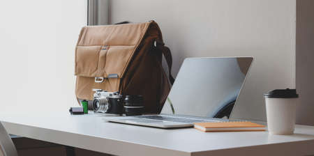 Comfortable workspace with open laptop computer with mailbag and office supplies next to the windowsの写真素材