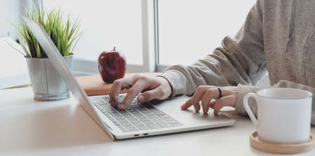 Close-up view of young female typing on laptop computer in comfortable workspace near the windows with coffee cupの写真素材