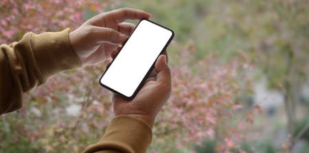 Close-up view of young man holding blank screen smartphone with garden blurred backgroundの写真素材