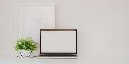 Simple workplace with minimalistic style with open blank screen laptop and mock up frameの写真素材