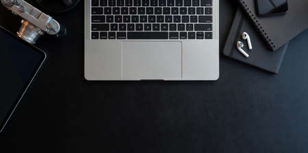 Top view of dark modern workplace with open laptop computer and office supplies on black leather desk backgroundの写真素材