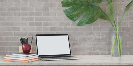 Loft workspace with open blank screen workplace with office supplies and tree pot on grey brick backgroundの写真素材