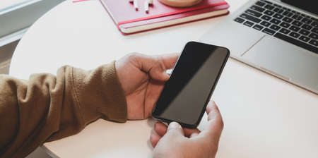 Cropped shot of man holding smartphone while working on his project in comfortable roomの写真素材