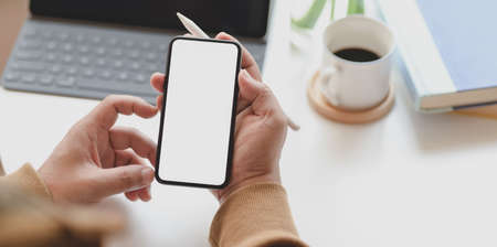 Close-up view of man holding blank screen smartphone while working on his projectの写真素材