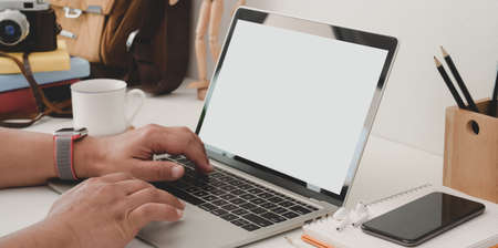Close-up view of young man typing on mock up laptop computer in modern workplace with office suppliesの写真素材