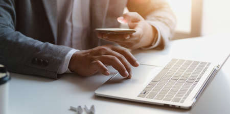 Close-up view of professional businessman looking at smartphone while working with laptop computer in his officeの写真素材