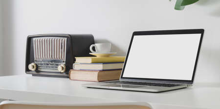 Minimal workspace with open blank screen laptop computer with office supplies and vintage radio and mock up frameの写真素材