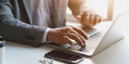 Close-up view of young businessman working on his project while typing on laptop computer in his office roomの写真素材