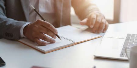 Close-up view of young professional businessman writing his idea concepts on notebook while working on his projectの写真素材