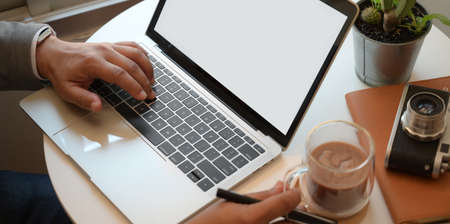 Close-up view of young businessman working with laptop computer while holding a cup of hot cocoaの写真素材