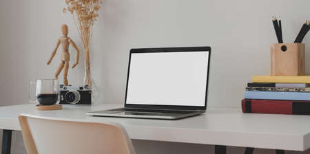Minimal office room with blank screen laptop computer with books and office supplies on white wooden tableの写真素材