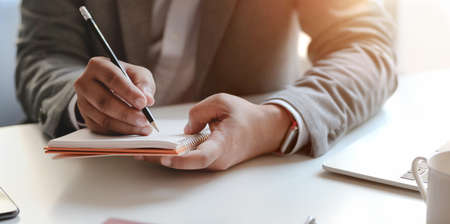 Close-up view of young professional businessman writing his idea concepts on notebook while working on his projectの写真素材