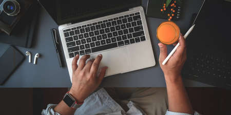 Top view of man working on his project with laptop computer while drinking a glass of orange juice in dark modern workspaceの写真素材