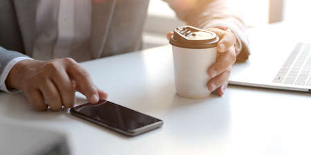 Cropped shot of professional businessman working on his project while touching his smartphone and holding a coffee cupの写真素材