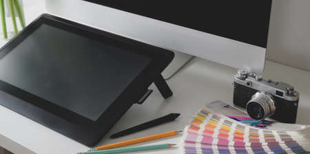 Close-up view of professional designer workspace with digital tablet, desktop computer and colour swatchesの写真素材