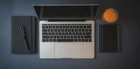 Top view of dark trendy workspace with mock up laptop computer and office supplies with orange juice on dark table backgroundの写真素材