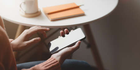 Cropped shot of young female holding smartphone in comfortable workplace near the windowsの写真素材