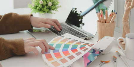 Cropped shot of young professional female designer choosing the colour for her project while typing on laptop computer の写真素材