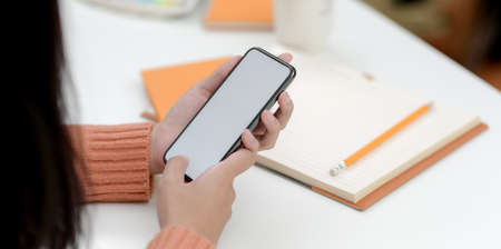 Close-up view of young female holding blank screen smartphone in comfortable office roomの写真素材