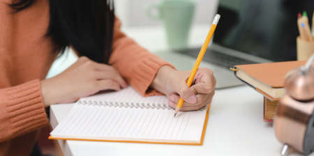 Cropped shot of young female writing her idea concepts on blank notebook in her modern workplace の写真素材
