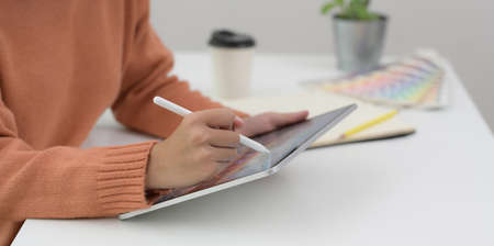 Cropped shot of young female working on her project with tablet in her comfortable workplaceの写真素材