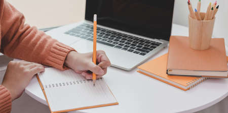 Close-up view of young woman working on her project while drafting her idea on notebook in comfortable workspaceの写真素材