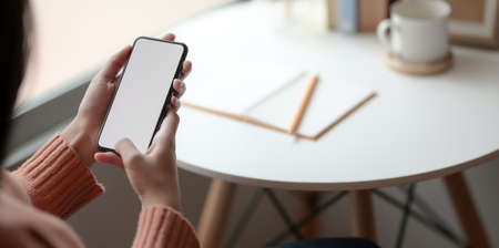 Close-up view of young female holding blank screen smartphone in comfortable office roomの写真素材