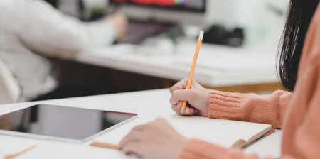 Close-up view of young female freelancer working on her project while writing her idea concepts on notebook の写真素材