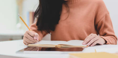 Close-up view of young female freelancer working on her project while writing her idea concepts on notebook の写真素材