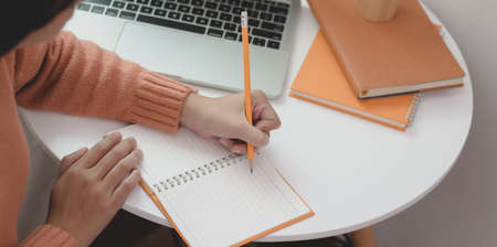 Close-up view of young woman working on her project while drafting her idea on notebook in comfortable workspaceの写真素材