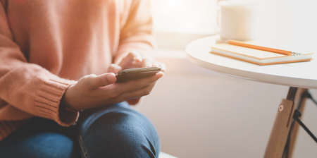 Cropped shot of young female holding smartphone in comfortable workplace near the windowsの写真素材