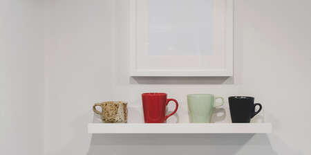 Cropped shot of wall shelf with coffee cups and mock up frame on white wall background の写真素材