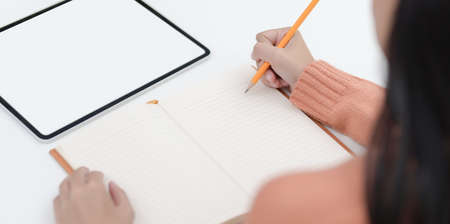 Close-up view of young female writing her idea on notebook while working on her project in comfortable room の写真素材