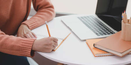Close-up view of young woman working on her project while drafting her idea on notebook in comfortable workspaceの写真素材