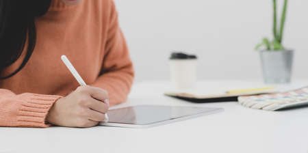 Close-up view of young female working on her project with tablet in her comfortable workplace の写真素材