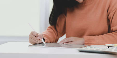 Close-up view of young female working on her project with tablet in her comfortable workplace の写真素材