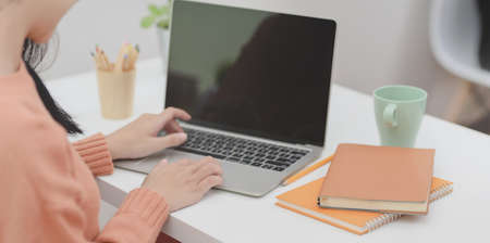 Cropped shot of young female typing on laptop computer while working on her project