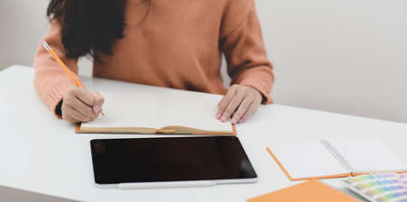 Cropped shot of young female freelancer working on her project with tablet and drafting her idea on notebook の写真素材