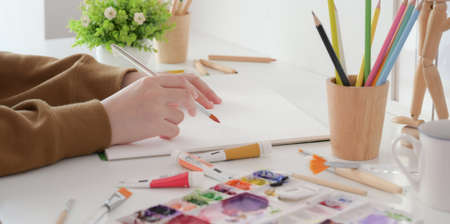 Close-up view of young female artist painting her project with water colour with painting brush in her studio の写真素材