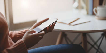 Close-up view of young female holding blank screen smartphone in comfortable office room