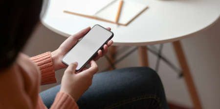 Close-up view of young female holding blank screen smartphone in comfortable office room