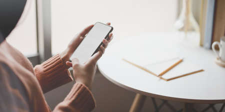 Close-up view of young female holding blank screen smartphone in comfortable office room