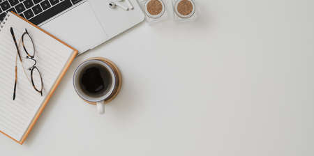 Top view of minimal workspace with laptop computer, a cup of coffee and office supplies on white desk background